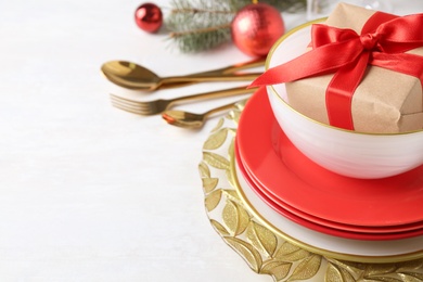 Photo of Festive dishware with gift and Christmas decorations on white table, closeup. Space for text