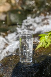 Photo of Wet glass of water on rocks near flowing stream outdoors