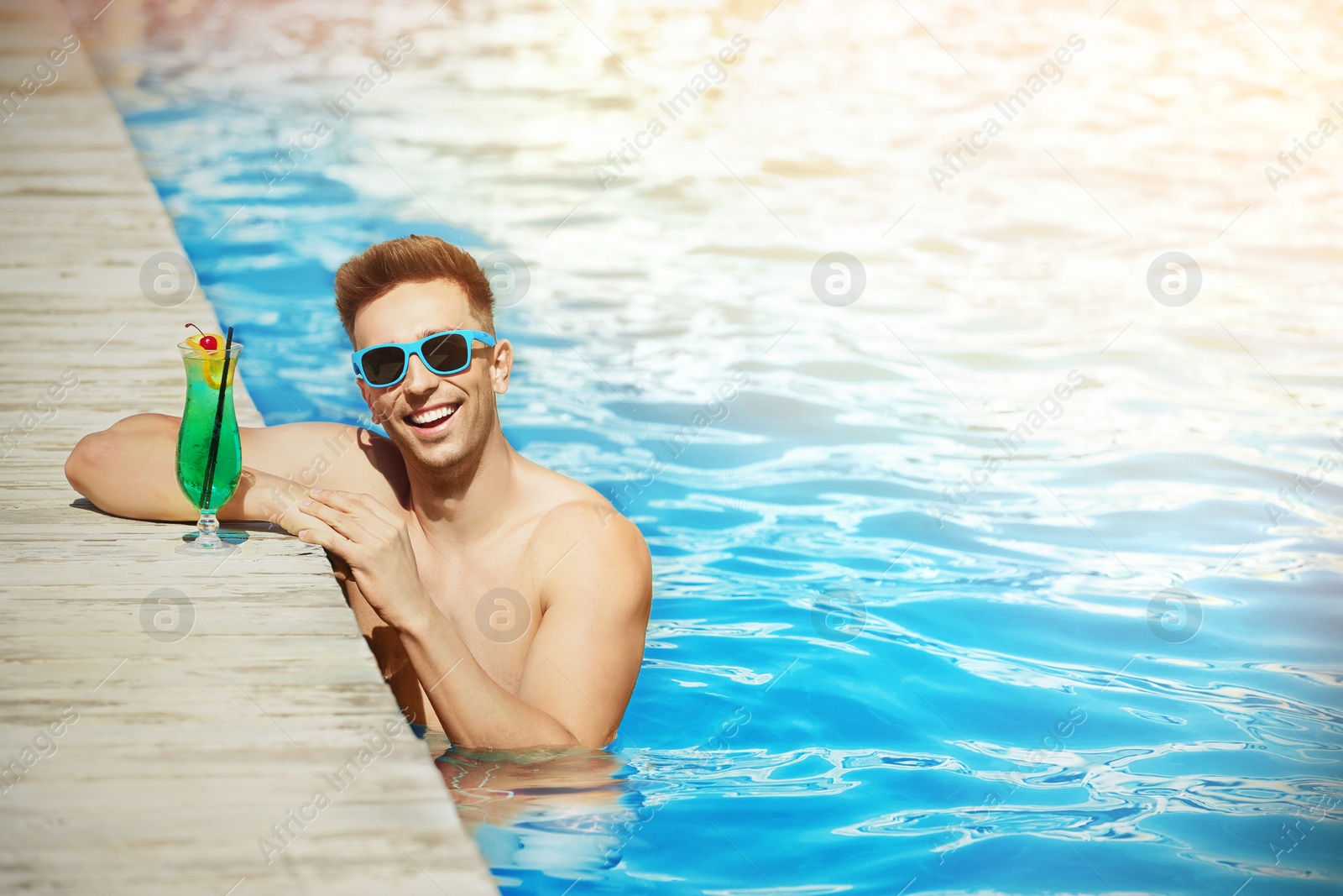 Image of Happy young man with cocktail in swimming pool