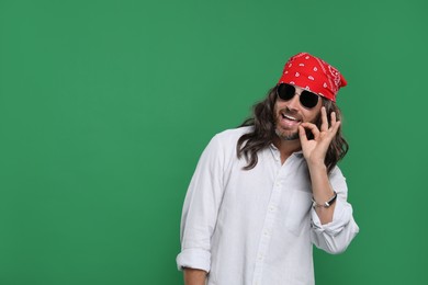 Stylish hippie man in sunglasses on green background, space for text