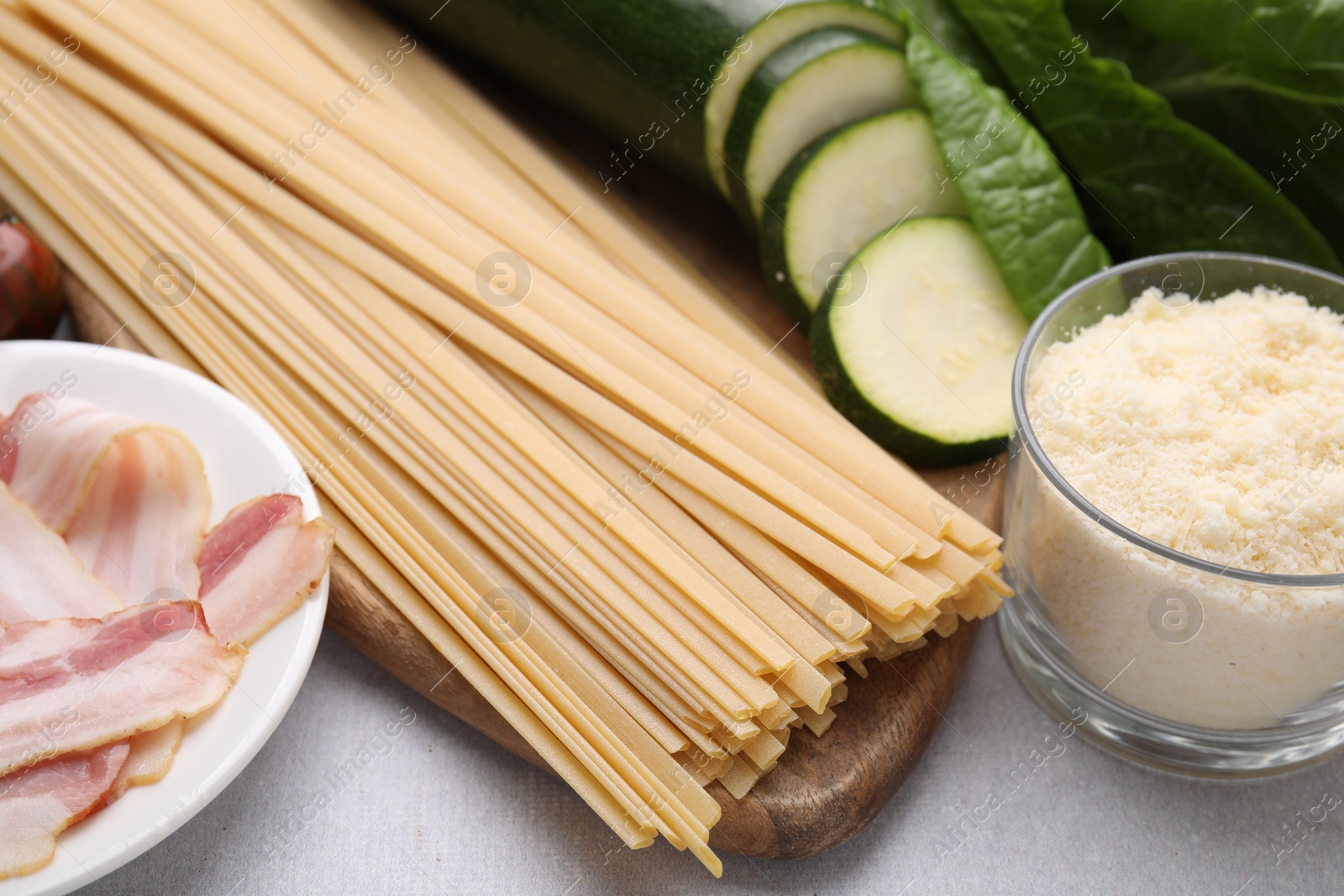 Photo of Raw pasta, bacon and fresh ingredients on light grey table