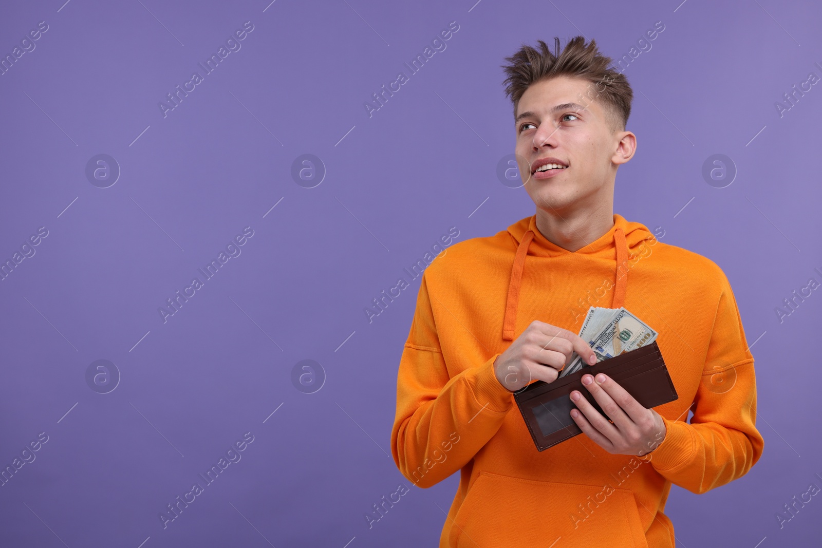 Photo of Happy man putting money into wallet on purple background. Space for text