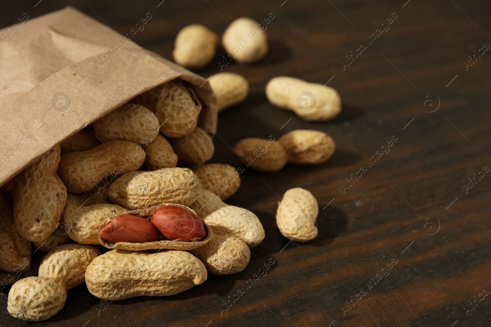 Photo of Paper bag with fresh unpeeled peanuts on wooden table, closeup. Space for text