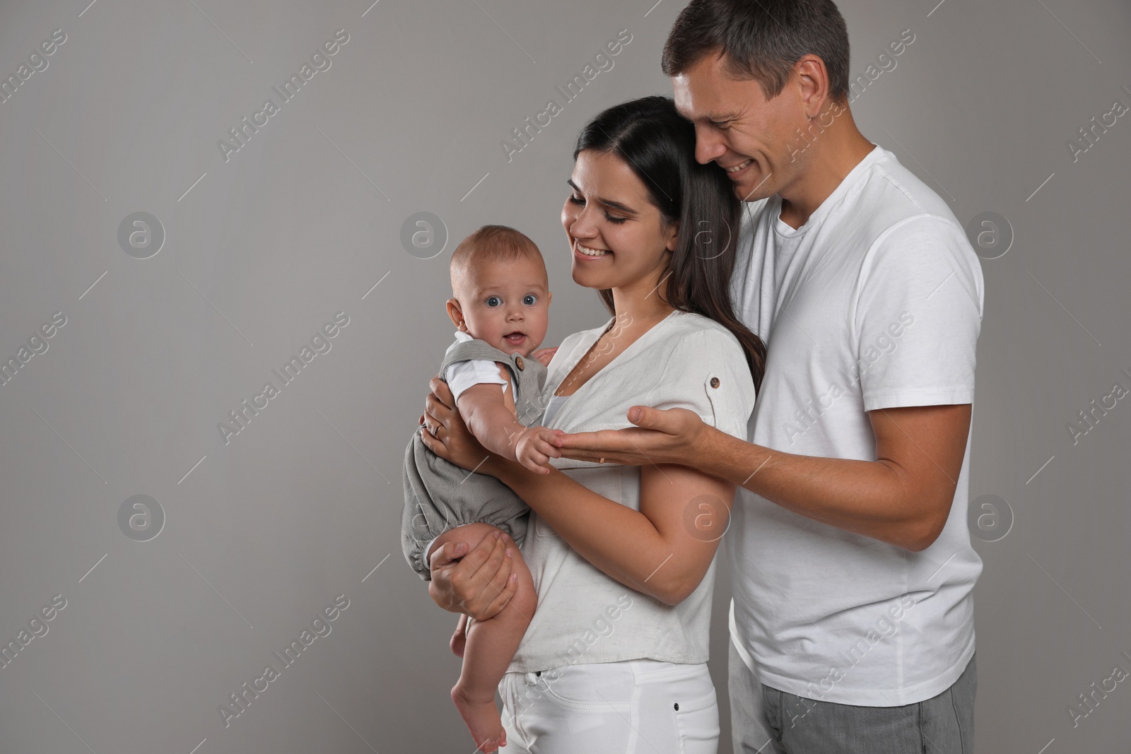 Photo of Happy family. Couple with their cute baby on grey background, space for text