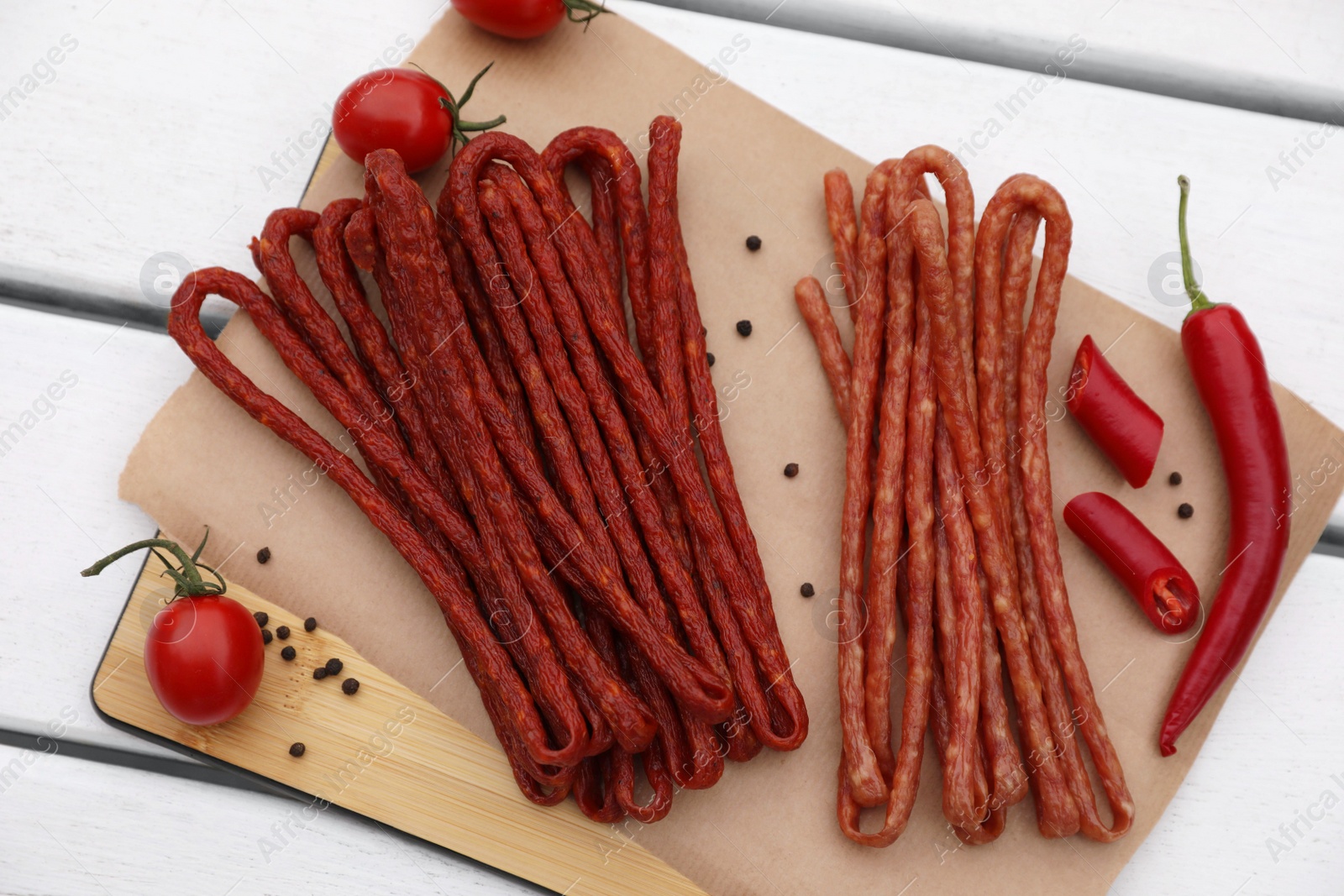 Photo of Delicious kabanosy with tomatoes, peppercorn and chilli on white wooden table, top view