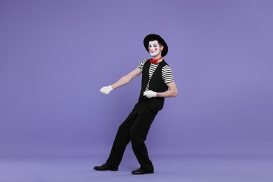 Funny mime artist in hat posing on purple background