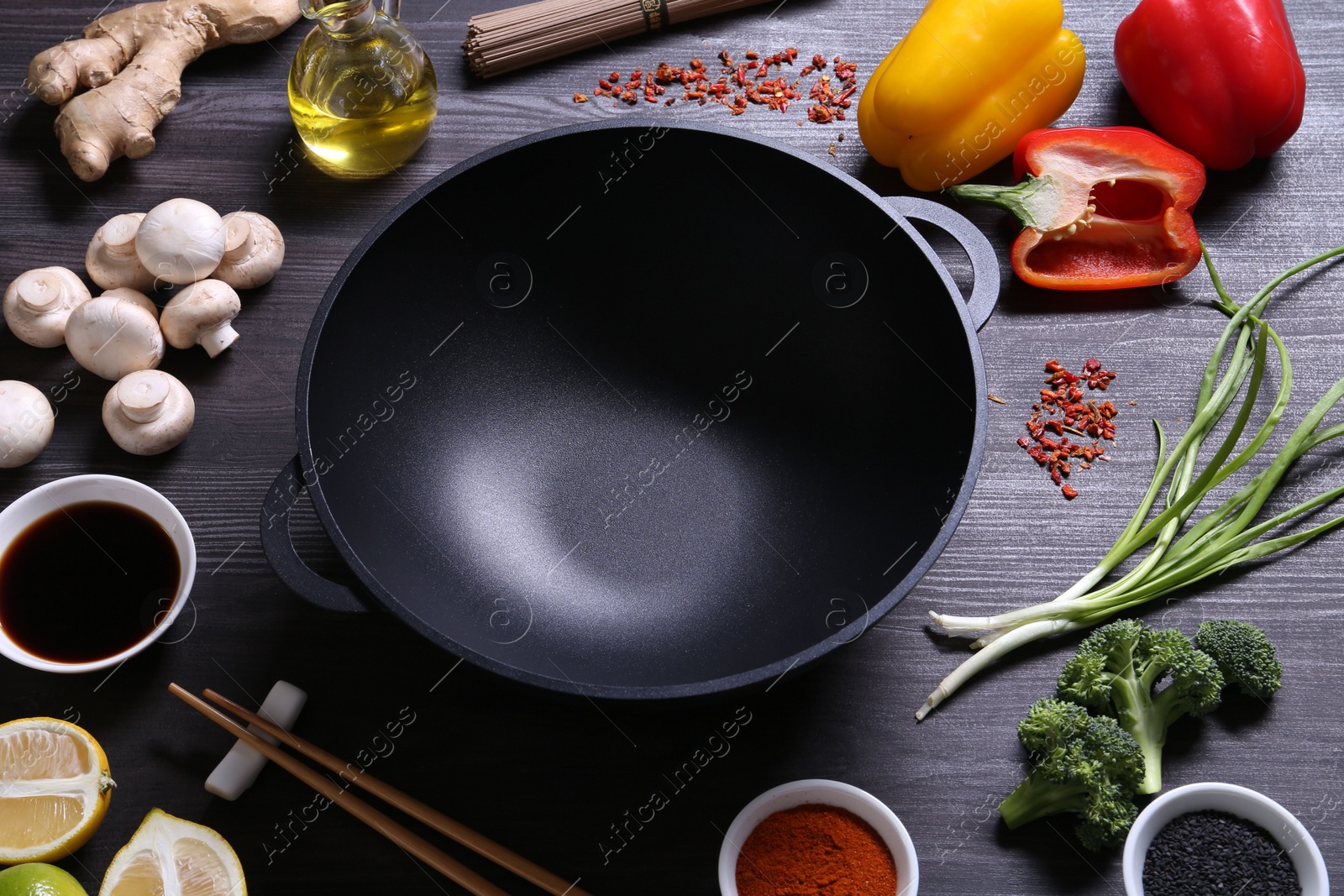 Photo of Empty iron wok and chopsticks surrounded by ingredients on dark grey wooden table