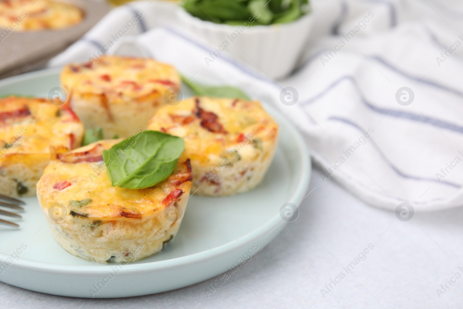 Photo of Freshly baked bacon and egg muffins with cheese on light gray table, closeup. Space for text