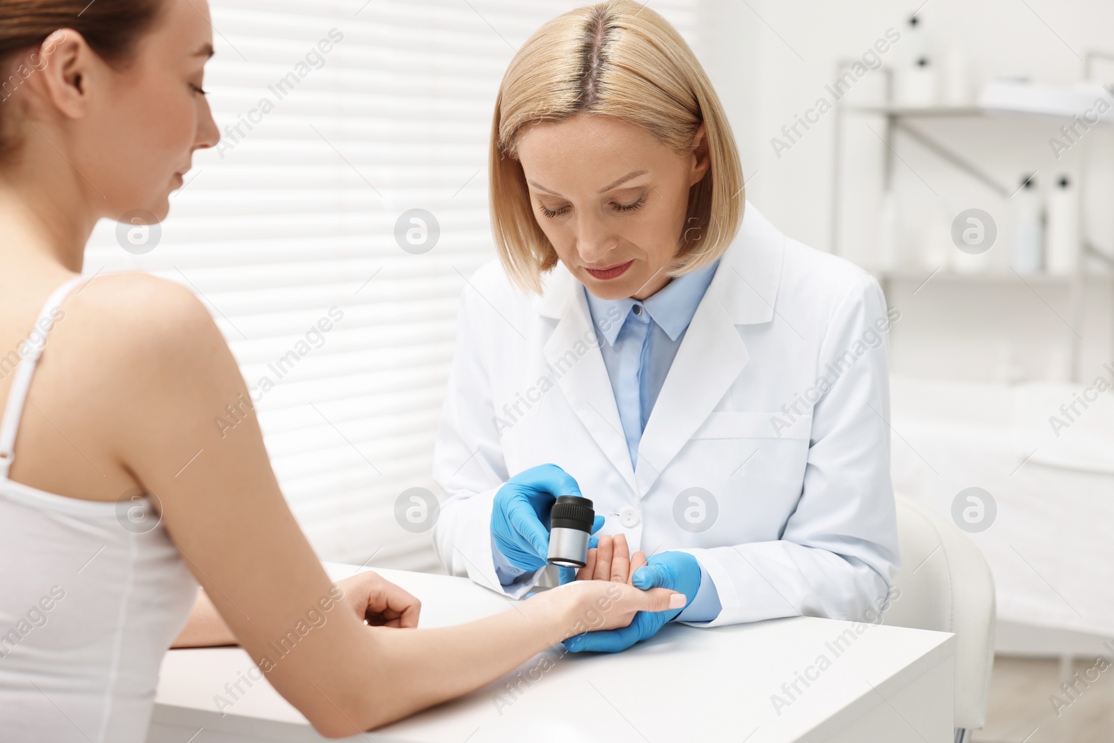 Photo of Dermatologist with dermatoscope examining patient at white table in clinic