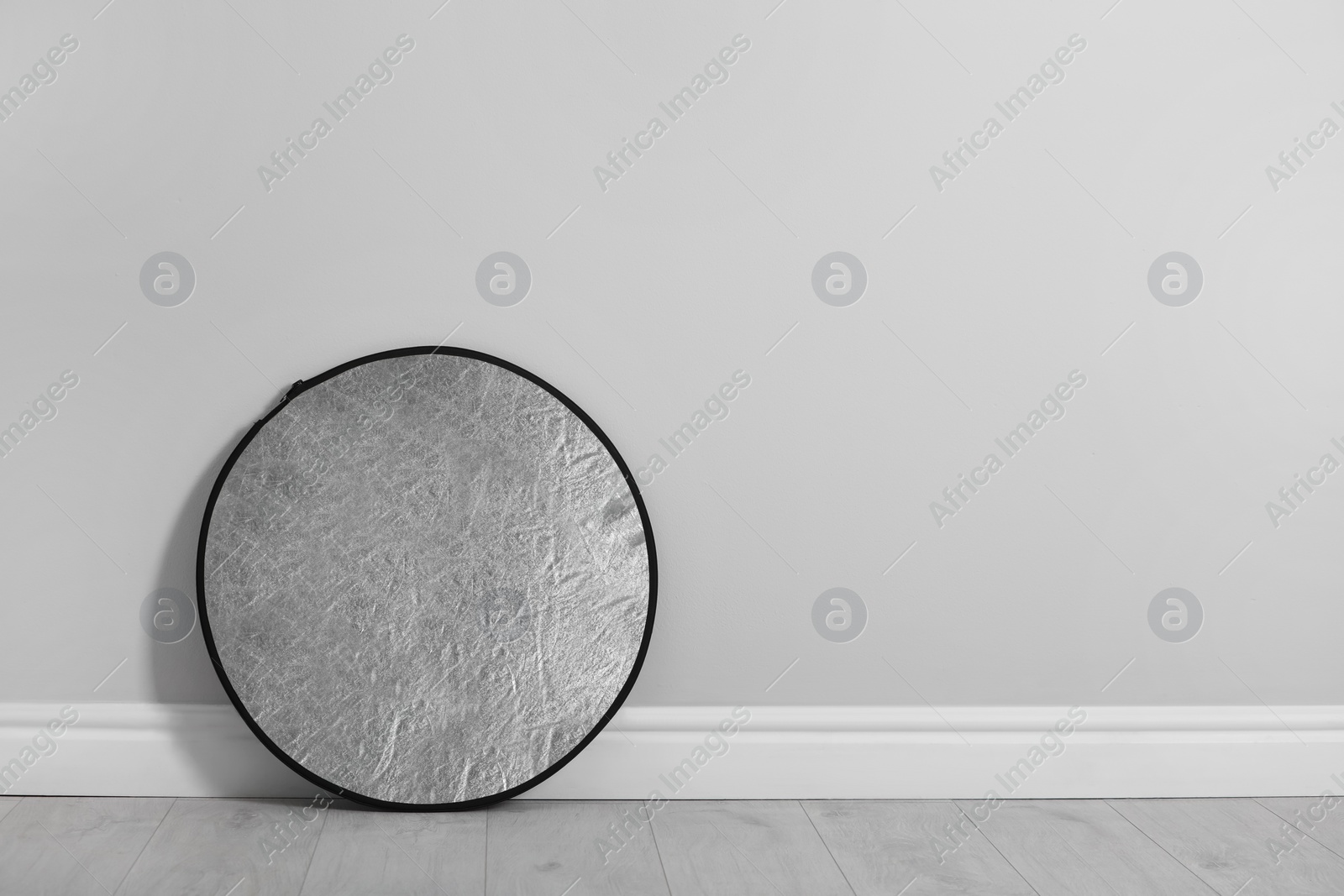 Photo of Studio reflector near grey wall in room, space for text. Professional photographer's equipment