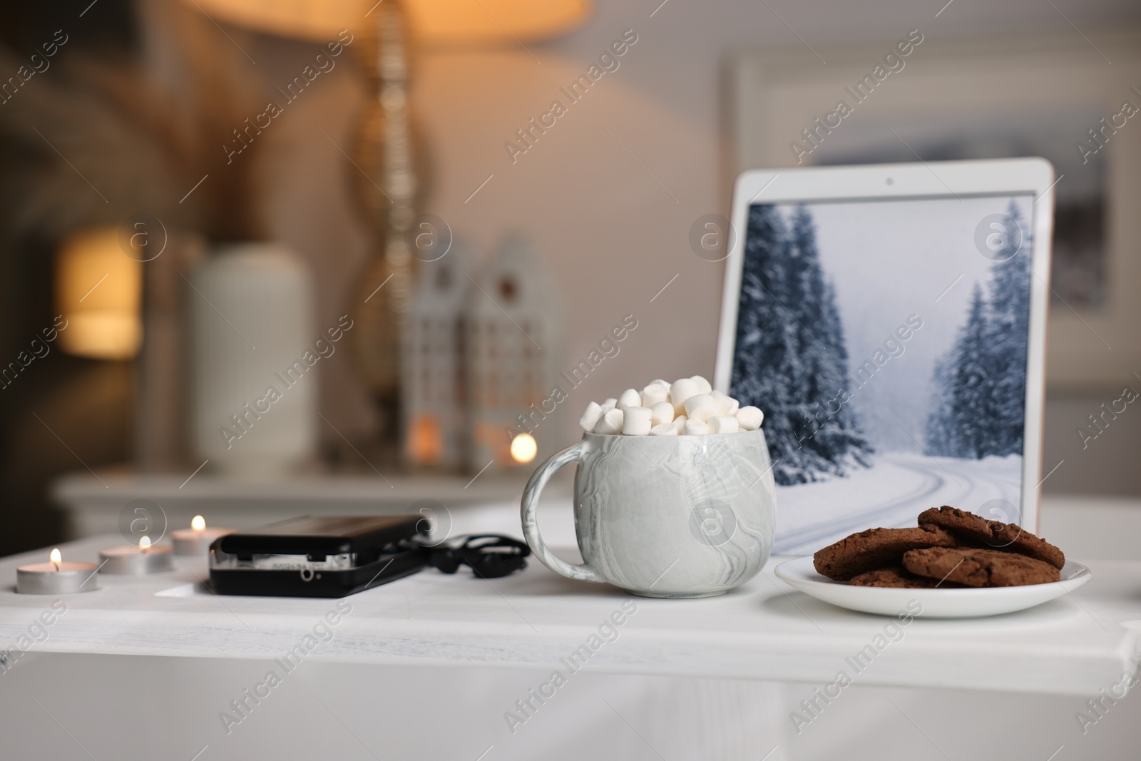 Photo of White wooden tray with tablet, cassette player, cookies and burning candles on bathtub in bathroom