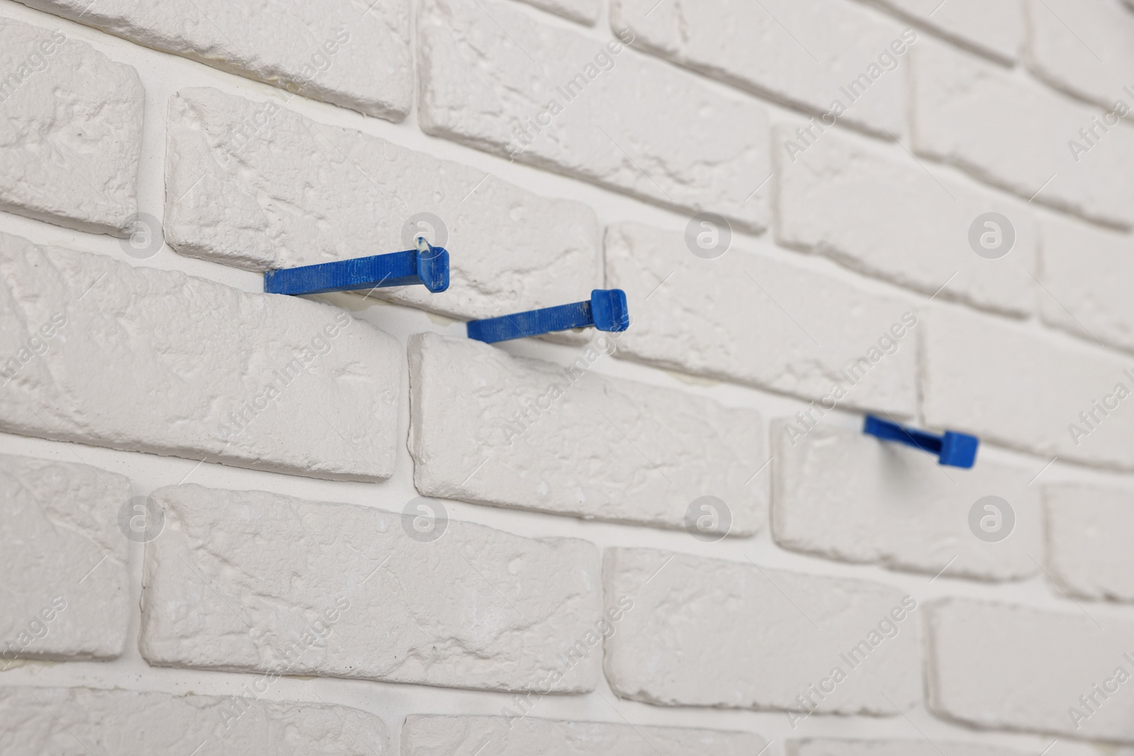 Photo of Decorative white bricks with tile leveling system on wall, closeup