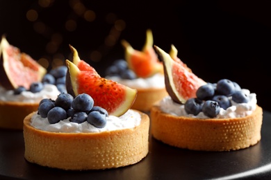 Photo of Tarts with blueberries and figs on black table against dark background, closeup. Delicious pastries