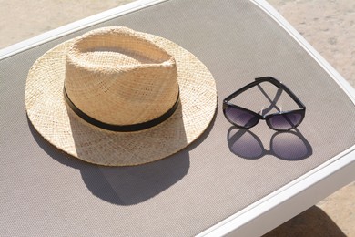 Stylish straw hat and sunglasses on grey sunbed outdoors. Beach accessories