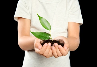 Child holding soil with green plant in hands on black background