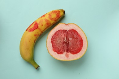 Photo of Banana with red lipstick marks and half of grapefruit on turquoise background, flat lay. Sex concept