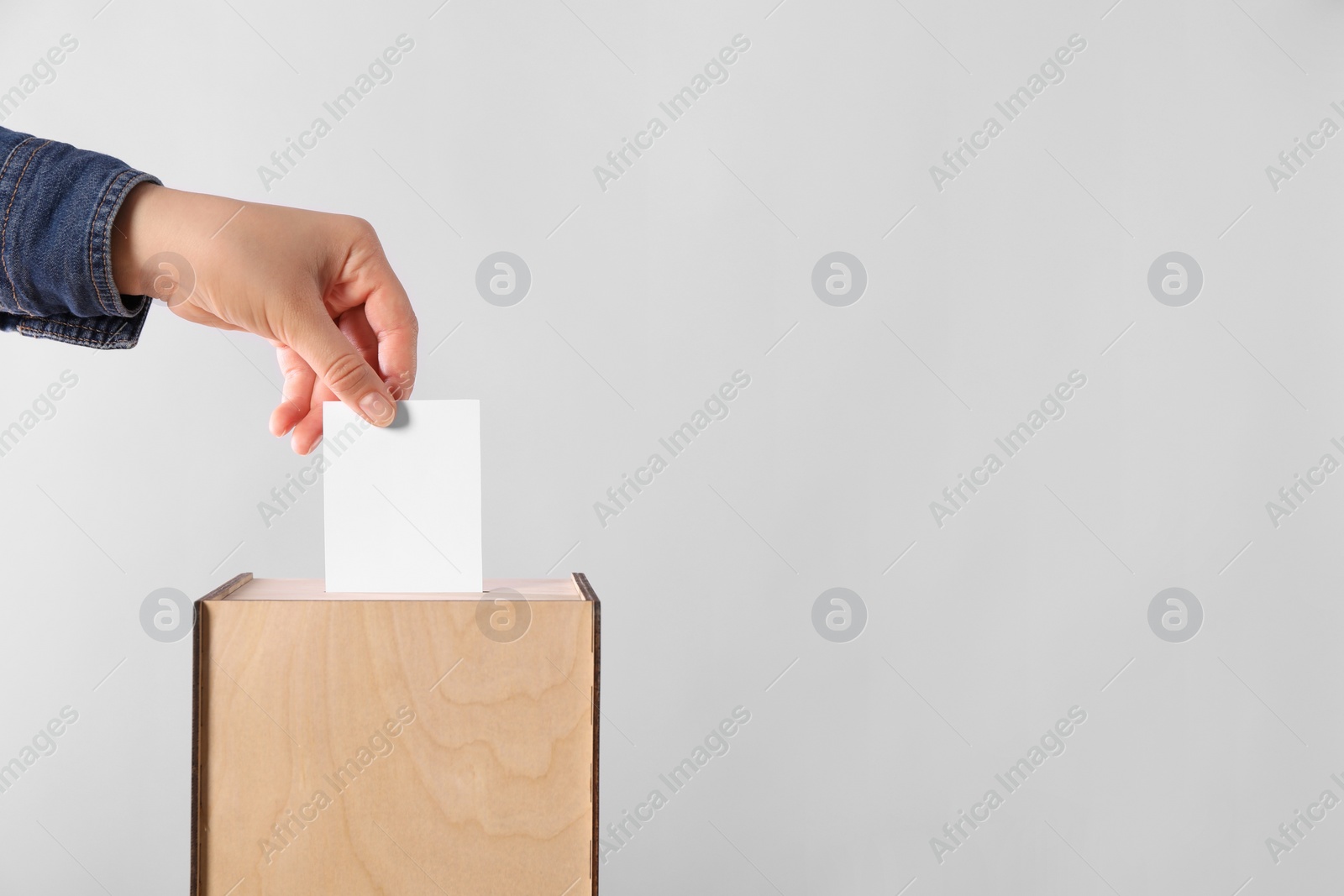 Photo of Woman putting her vote into ballot box on light grey background, closeup. Space for text