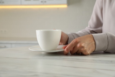 Photo of Woman with white cup and saucer at table indoors, closeup