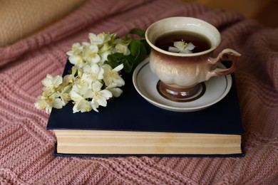 Photo of Cup of aromatic tea, beautiful jasmine flowers and hardcover book on pink fabric