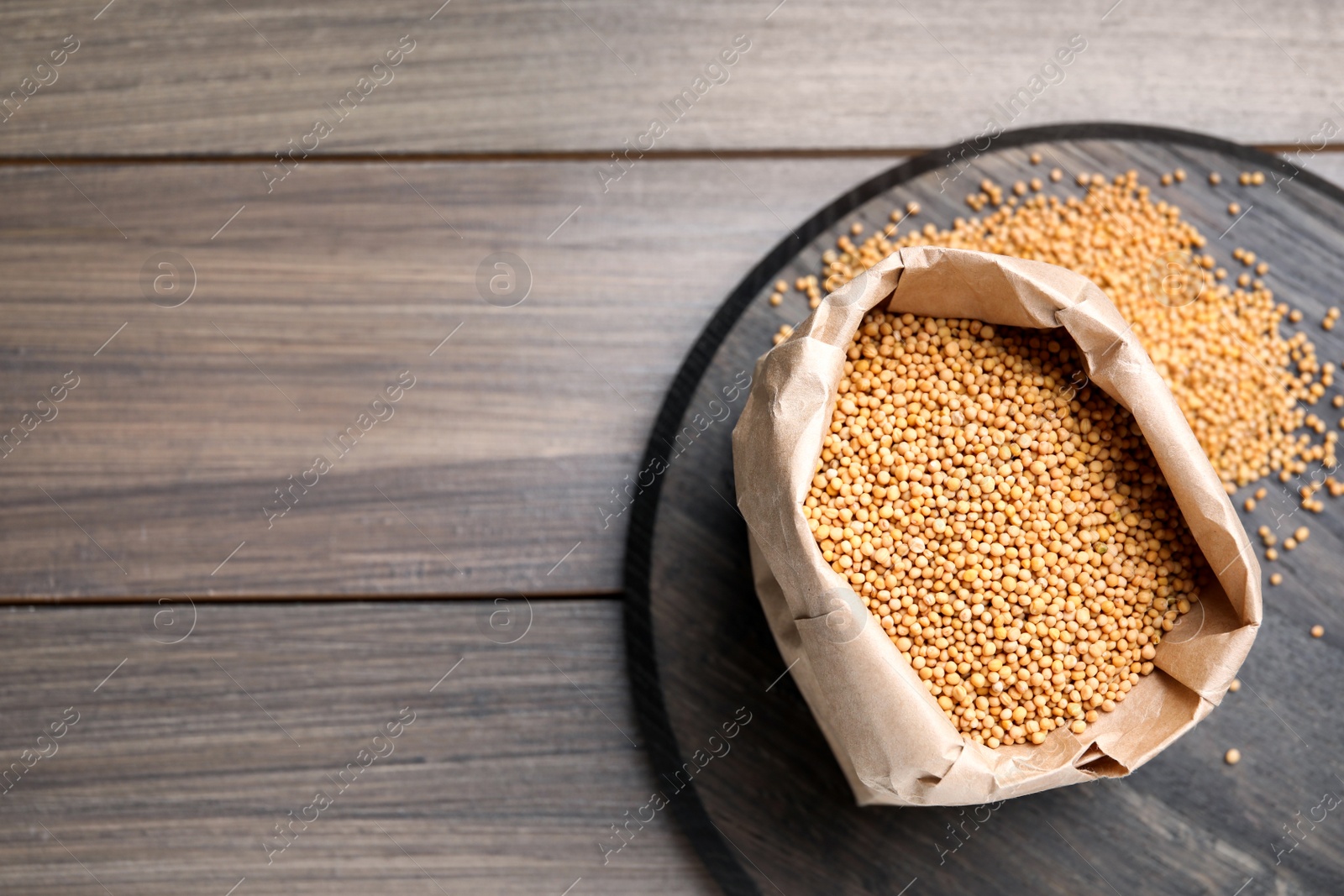 Photo of Mustard seeds in paper bag on wooden table, flat lay. Space for text