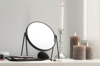 Photo of Dressing table with mirror, cosmetic products and burning candles in makeup room