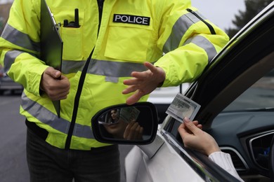 Photo of Police officer rejecting bribe near car outdoors, closeup
