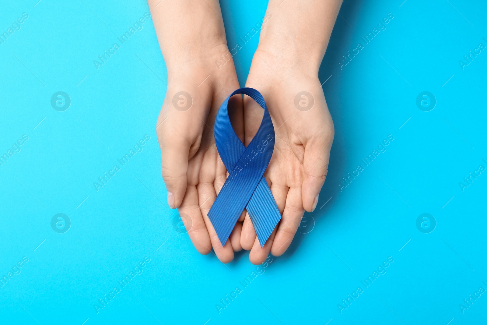 Photo of Woman holding blue awareness ribbon on color background, top view. Symbol of social and medical issues