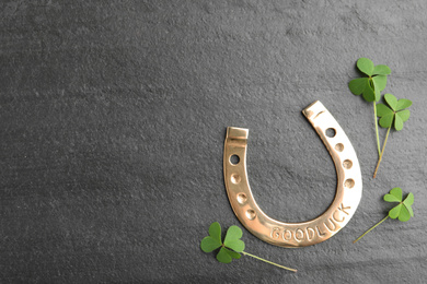 Photo of Clover leaves and horseshoe on grey stone table, flat lay with space for text. St. Patrick's Day celebration