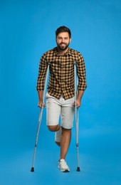 Young man with injured leg using axillary crutches on light blue background