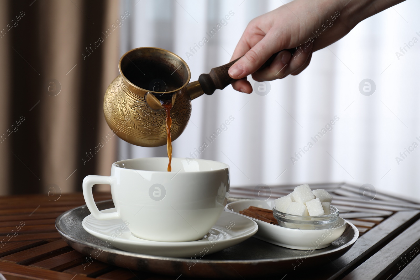 Photo of Turkish coffee. Woman pouring brewed beverage from cezve into cup at wooden table, closeup