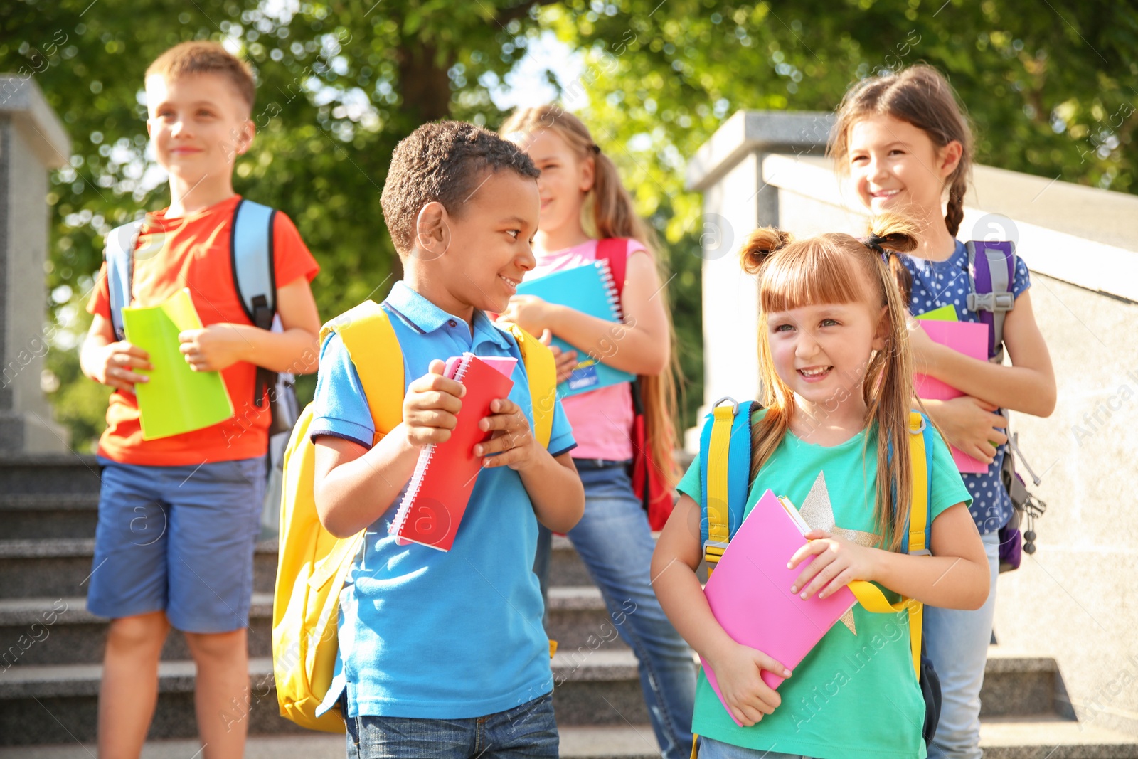 Photo of Cute little children with backpacks and notebooks outdoors. Elementary school