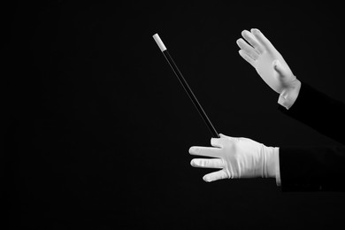 Photo of Magician holding wand on black background, closeup. Space for text