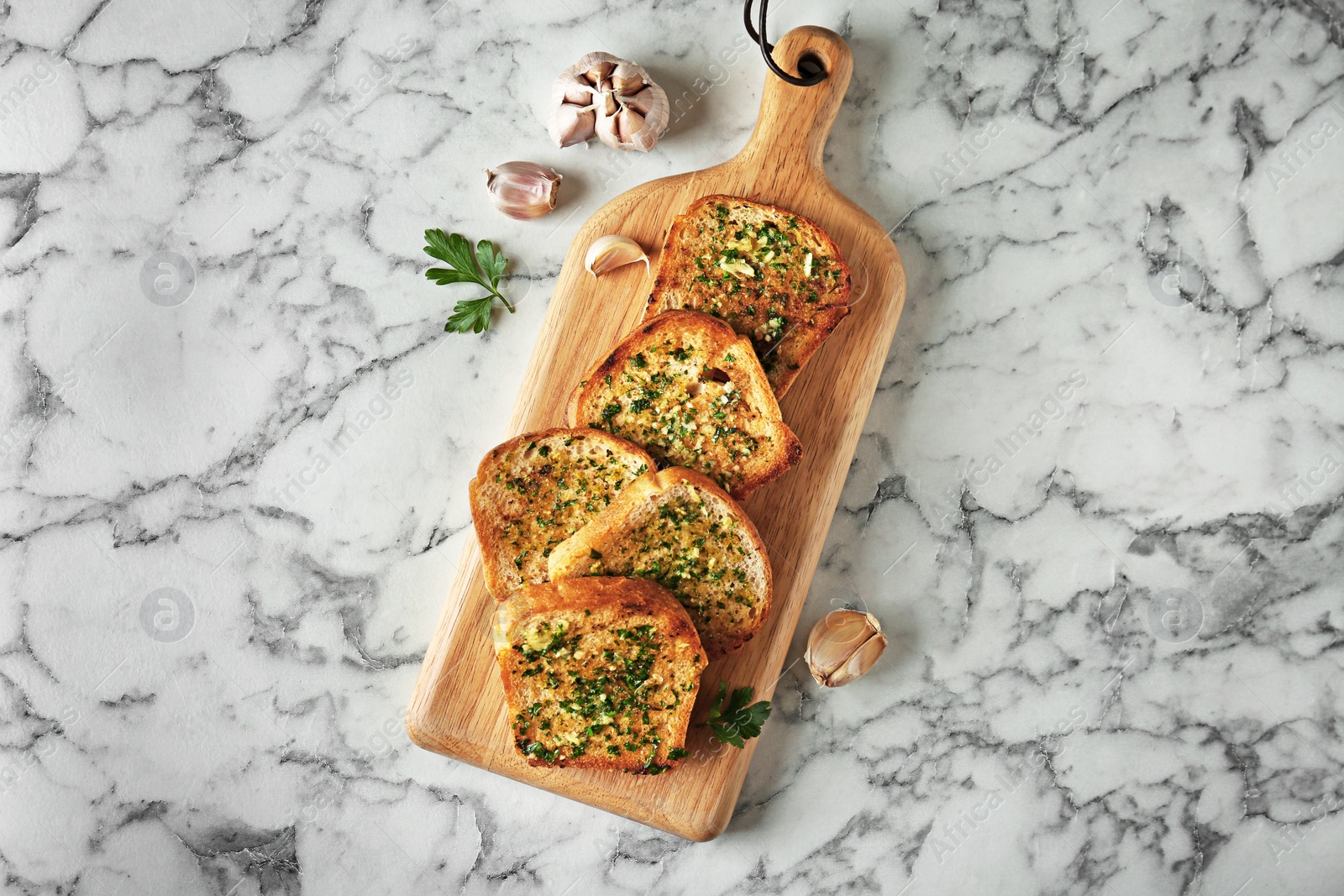 Photo of Slices of toasted bread with garlic and herbs on marble table, flat lay