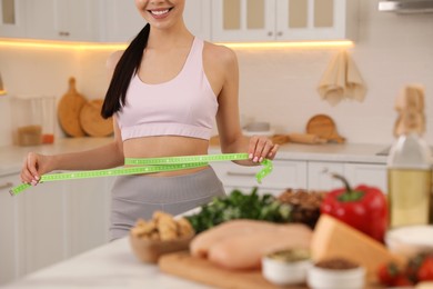 Happy woman measuring waist with tape in kitchen, closeup. Keto diet