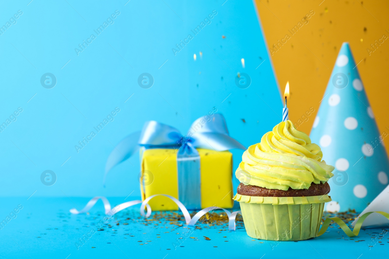 Photo of Delicious birthday cupcake with candle, near gift box and party hat on light blue background, space for text