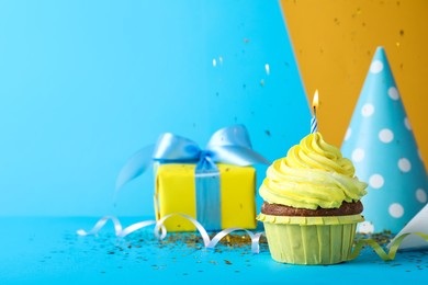 Photo of Delicious birthday cupcake with candle, near gift box and party hat on light blue background, space for text