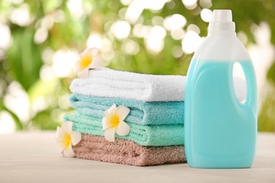 Photo of Pile of fresh towels, flowers and detergent on table against blurred background