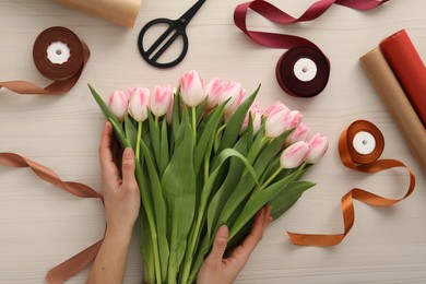 Woman making bouquet of beautiful fresh tulips at white wooden table, top view