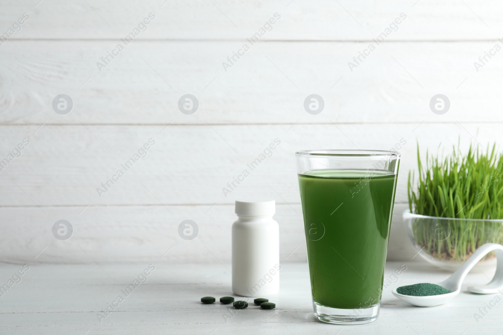 Photo of Glass of spirulina drink, pills and powder on table. Space for text