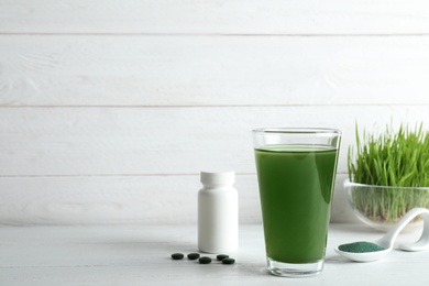 Photo of Glass of spirulina drink, pills and powder on table. Space for text