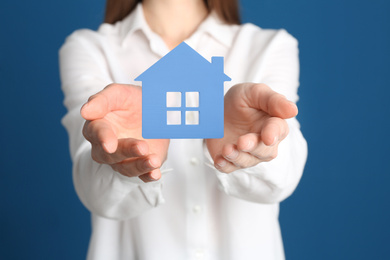 Image of Home security concept. Woman holding house on blue background, closeup