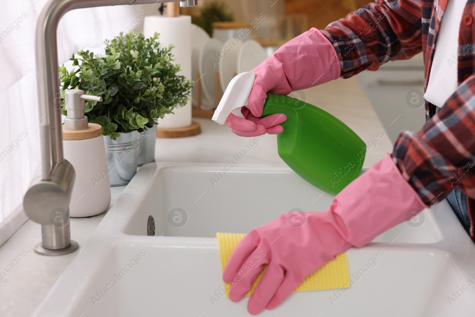 Photo of Woman with spray bottle and microfiber cloth cleaning sink in kitchen, closeup