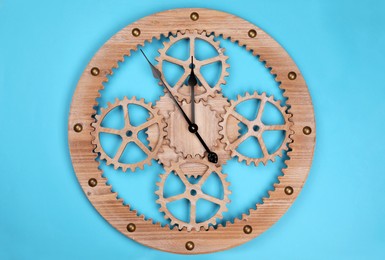 Photo of Stylish wall clock with gears showing five minutes until midnight on light blue background, top view. New Year countdown