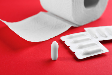 Photo of Suppositories and toilet paper on red background. Hemorrhoid treatment