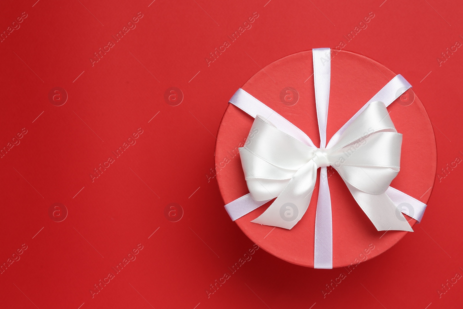 Photo of Beautiful gift box with white bow on red background, top view. Space for text