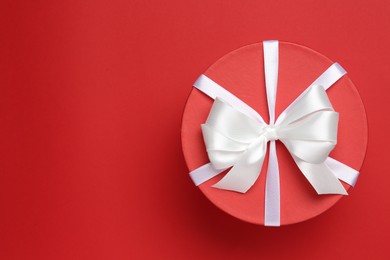 Photo of Beautiful gift box with white bow on red background, top view. Space for text