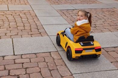 Cute little girl driving children's car on city street. Space for text