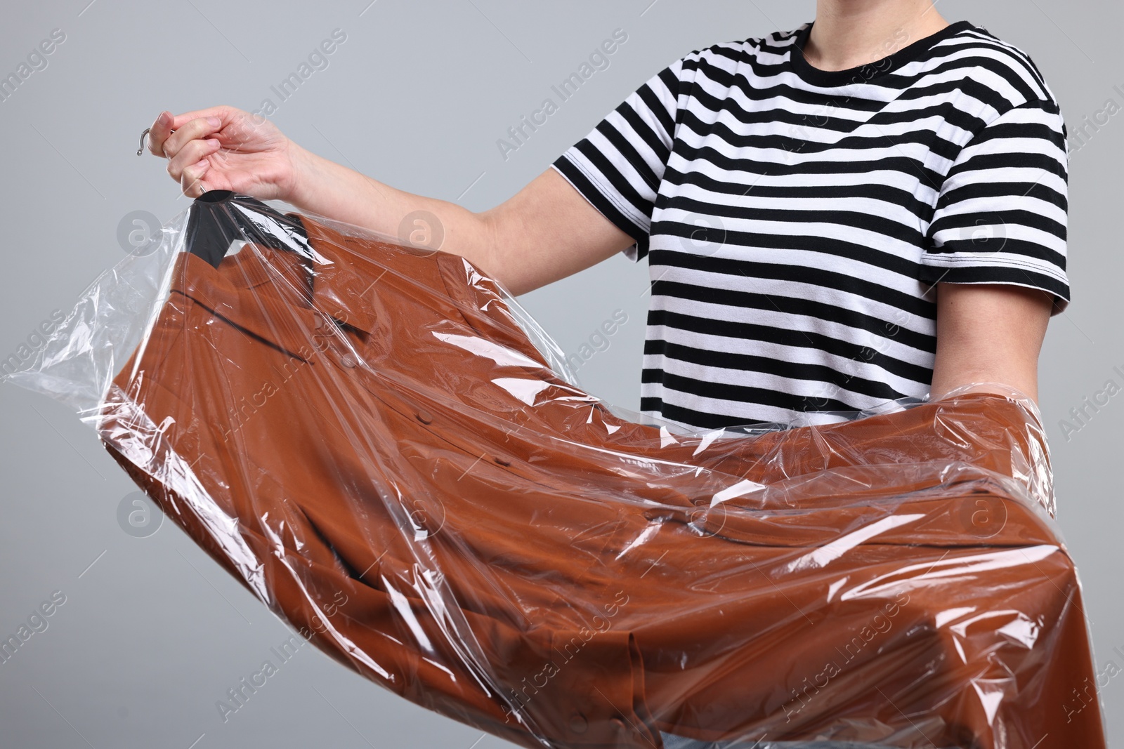 Photo of Dry-cleaning service. Woman holding shirt in plastic bag on gray background, closeup