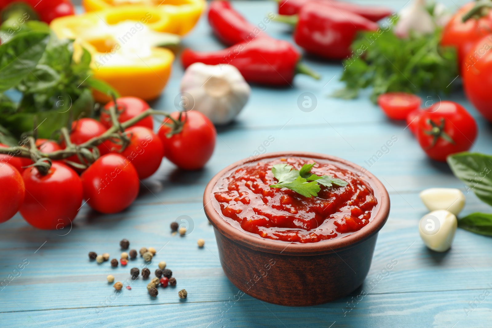 Photo of Delicious adjika sauce in bowl and ingredients on light blue wooden table