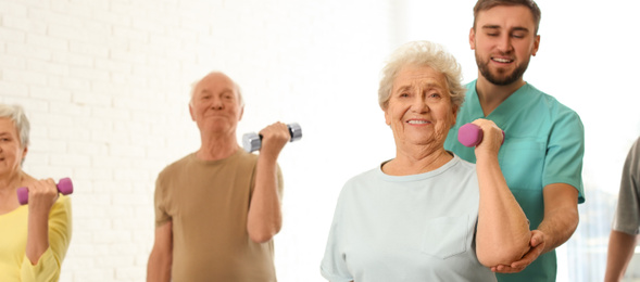Image of Care worker helping elderly woman to do exercise with dumbbell in hospital gym. Banner design